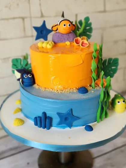 A Finding Nemo themed cake for a girl named Nimo. This two-tier cake features two flavors, chocolate mousse and pineapple, and is decorated with characters like Nemo and Dory in an underwater scene.