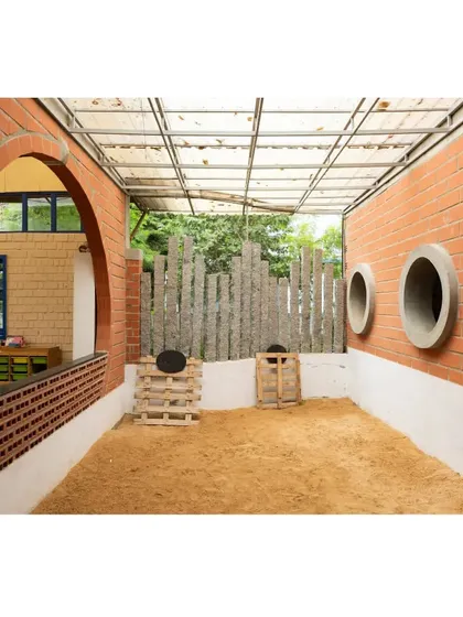Even small, transitional spaces are designed for activity. This outdoor sandpit, enclosed by brick walls with circular cutouts, provides a dedicated area for sensory play that is safely integrated into the building's design.