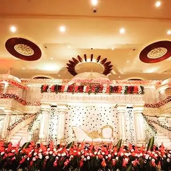 An exceptionally grand wedding stage design in white and red. The setup features majestic pillars, intricate latticework, and a profusion of red gladiolus flowers, creating a palatial feel for the ceremony.