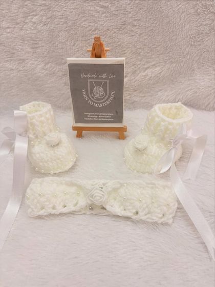 A clear, full view of the handmade crochet booties and headband set, showing the delicate rose and pearl details against the soft white yarn.