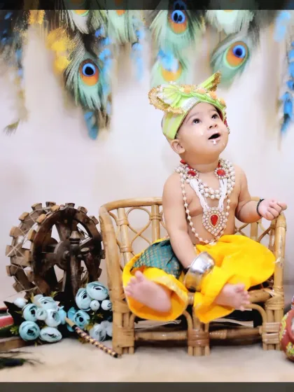 Looking up in wonder, this little Krishna enjoys his time in our specially designed wicker chair, set against a backdrop of peacock feathers.