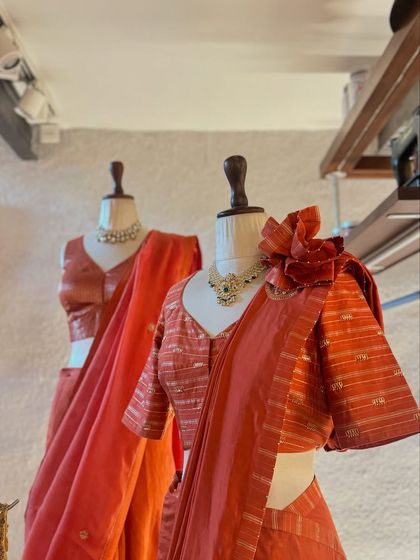 Two beautiful sarees in shades of orange, one with a statement floral appliqué on the shoulder, showcasing unique design elements.