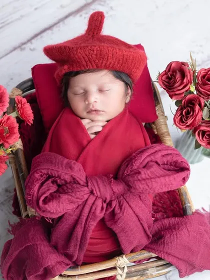 A pop of red! This newborn looks striking in a red wrap and hat, nestled in a basket.