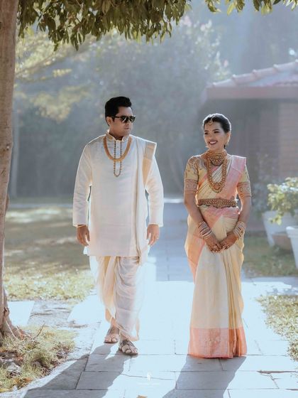 A stylish shot of the couple walking together after their ceremony. The groom's sunglasses add a modern touch to their traditional attire.