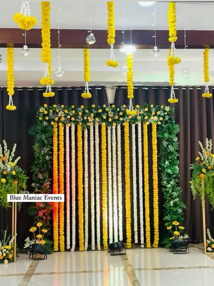 A beautiful Haldi stage with a backdrop of hanging marigold garlands and lush green floral pillars.