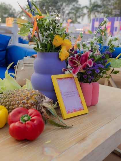 An outdoor lounge area with bright blue couches and colorful cushions. The tables are decorated with sustainable centerpieces made from fresh fruits, vegetables, and flowers.