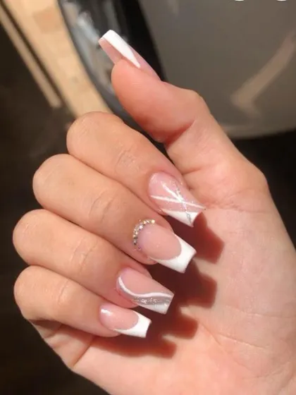 A sharp and modern take on the French manicure. This set features a deep V-cut white tip on a square nail, with abstract white lines and a rhinestone accent.