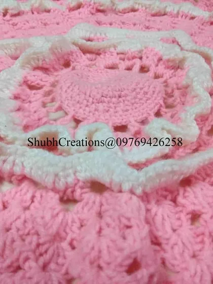 A close-up of a delicate pink and white crochet piece, perfect for a baby blanket or a decorative table mat. This design teaches you how to work in the round and create beautiful layered effects.