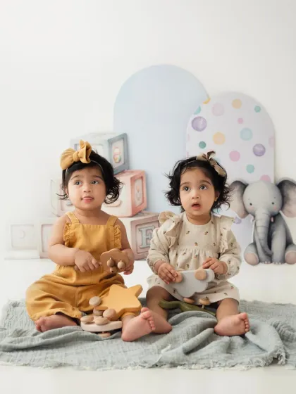 Twin sisters sit together with their wooden toys in a pastel-colored studio setup. A sweet portrait from a twin sitter session.