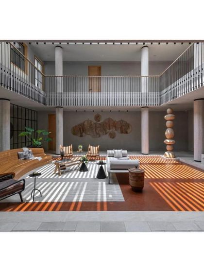 The central courtyard of the K House, a double-height space that serves as the heart of the home. Sunlight filters through, creating dynamic patterns on the floor, highlighting the blend of contemporary furniture and traditional architectural forms.