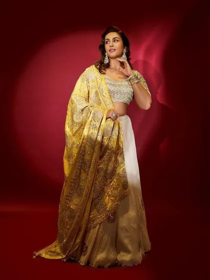 A gorgeous Faabiiana official lehenga in gold and off-white. The heavily embroidered yellow dupatta adds a pop of color, making it a great choice for a Dussehra celebration or festive event.