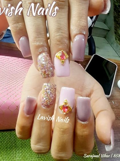 A regal design with nude pink nails, gold glitter, and a large, eye-catching pink and gold jewel accent.