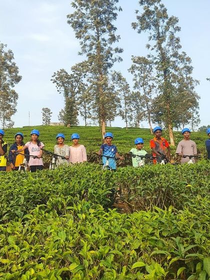 Young cyclists from the KRIES camp pose for a photo amidst the lush tea gardens of Barapole.