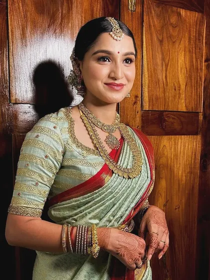 A bride in a sage green and red Kanchipuram saree. Her custom blouse features delicate line embroidery, creating a modern and subtle texture.
