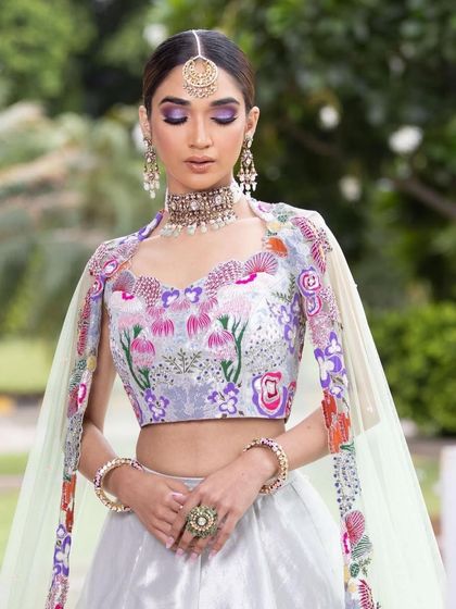 A dreamy and romantic look for a Mehendi or engagement. The makeup features a purple smokey eye and glowing skin, complementing the pastel floral outfit.
