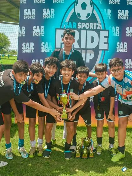 A team celebrates their Pride Cup victory with their coaches, holding their trophy and medals.