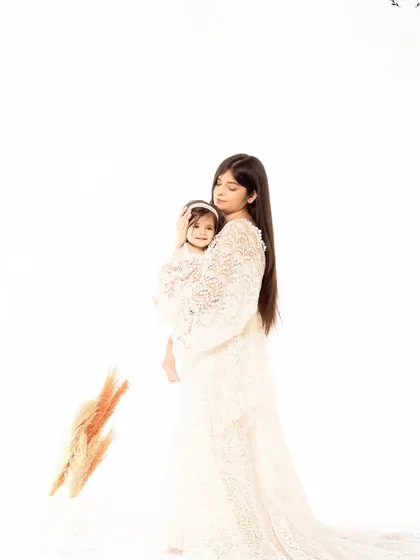 A mother holds her daughter close in a tender embrace. The soft, high-key lighting and their matching lace outfits create a delicate and angelic mother-daughter portrait.