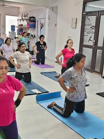 A group of women practicing a kneeling pose to strengthen their quadriceps and improve balance. The focus and determination in the room are inspiring.