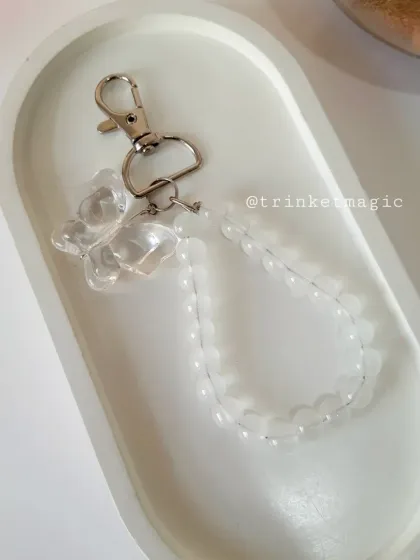 A clear beaded bag charm with a matching clear butterfly. This versatile piece adds a touch of sparkle without clashing with any color.