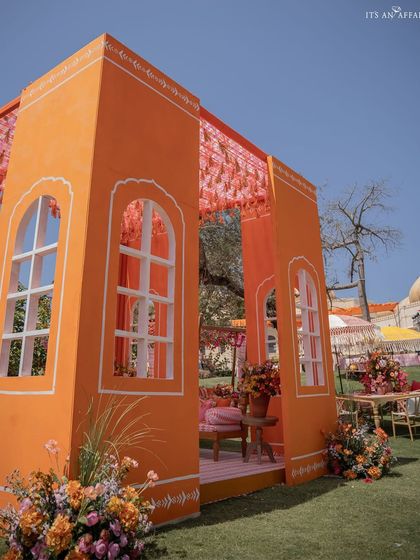 A custom-built structure resembling a traditional Punjabi house facade in bright orange, creating an immersive and thematic photo backdrop.