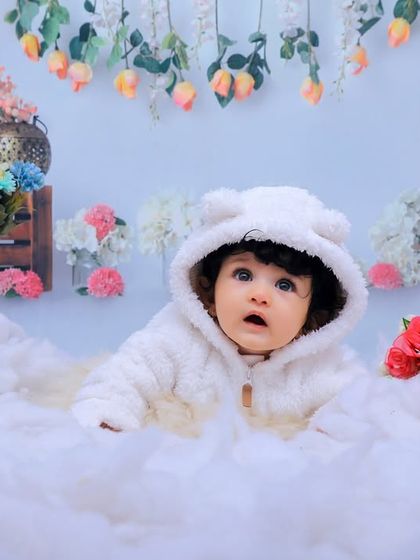 A baby wearing a fluffy bear-eared hoodie peeks out from a bed of soft white "snow." Our winter wonderland theme is perfect for cozy and cute portraits.