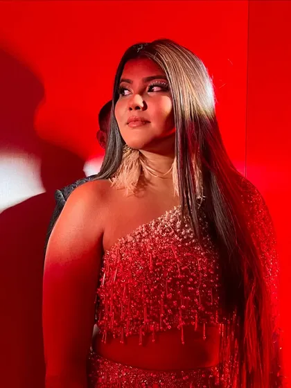 A close-up under dramatic red lighting. Her makeup holds up beautifully, with the highlighter catching the light for a stunning effect.