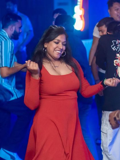 A woman in a red dress lighting up the dance floor with her smile and moves.