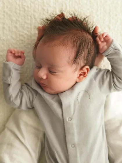 A close-up of a newborn's sleepy face and spiky hair, with their tiny fists raised. I love capturing these quirky and adorable details.
