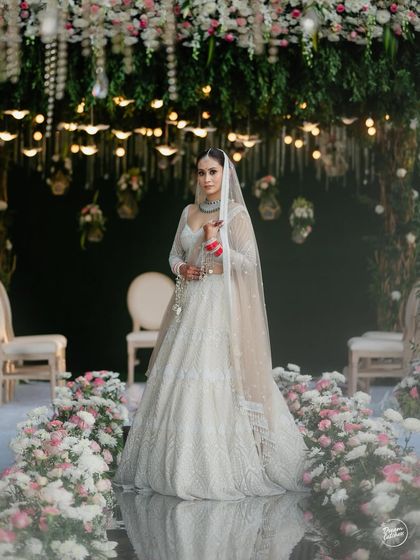 A bride stands on a mirror aisle, surrounded by our pastel floral arrangements. The decor creates a magical, reflective path leading to a beautifully adorned mandap.