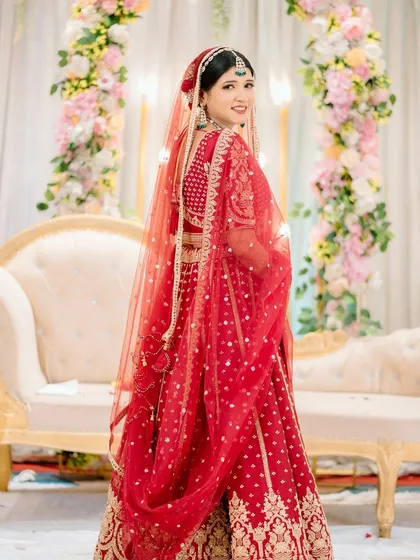 A beautiful three-quarter length portrait of the bride, with her looking back over her shoulder. The red of her lehenga is vibrant against the soft background.