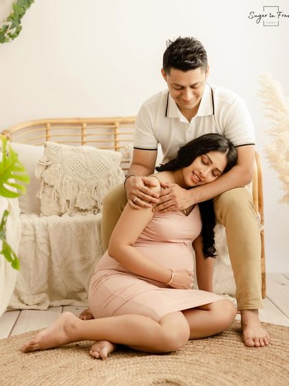A tender moment from a boho maternity shoot, where the expecting mother rests comfortably in her partner's arms. The soft lighting and natural textures create a peaceful atmosphere.