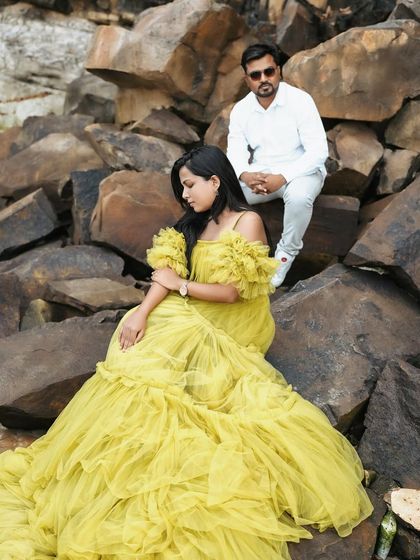 A couple's pre-wedding shoot in a rocky, natural landscape. The woman's bright yellow ruffled gown creates a stunning contrast with the surroundings.