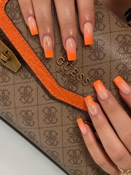 A bold and fiery sunset ombré with long, square-shaped extensions. The vibrant orange fades into a soft nude base, with a touch of gold glitter for extra flair.