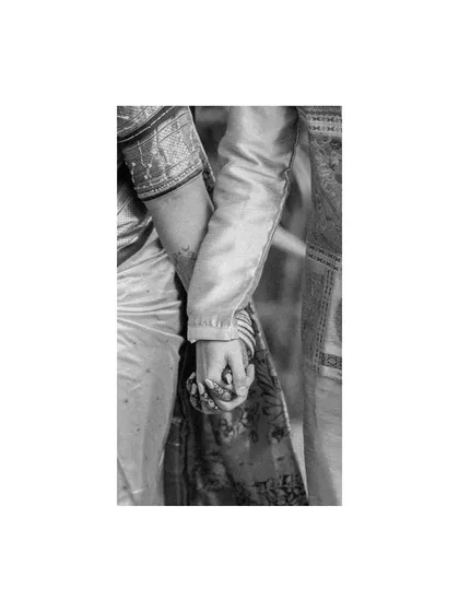 A black and white detail shot of the couple holding hands, focusing on the bride's bangles and the groom's traditional attire.