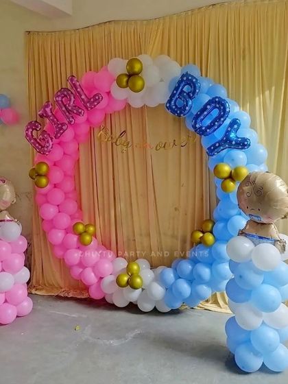 A gender reveal baby shower decoration with a pink and blue balloon ring. Foil balloons spelling 'GIRL' and 'BOY' make the theme clear and fun.