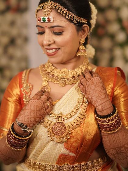 A stunning South Indian bride, Harshitha, adorned in gold jewelry that beautifully complements her dark henna stain.