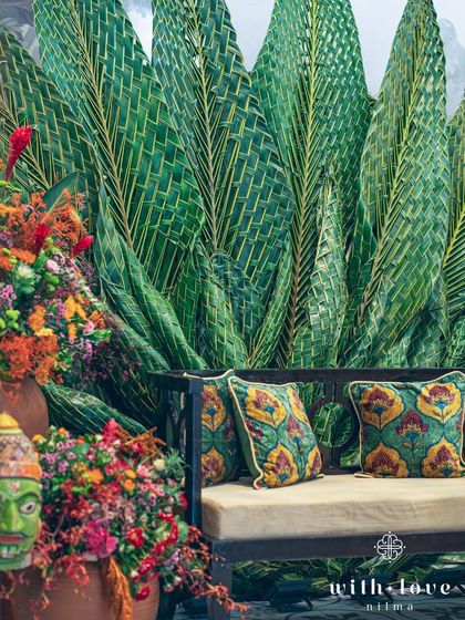 A detail of the Pellikuthuru decor, with a traditional mask and vibrant floral arrangements set against the woven coconut leaf backdrop.