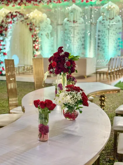 A close-up of the floral arrangements on a curved, marble-top table, featuring deep red and white flowers.