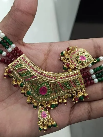 A close-up of a Jadau jewellery choker with intricate green and red meenakari work. This is a classic piece for a traditional look.
