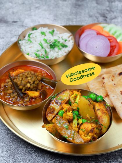 Wholesome goodness in a vegetarian thali. This plate features aloo gobi matar, whole lentil curry, rice, and roti, a classic North Indian comfort meal.