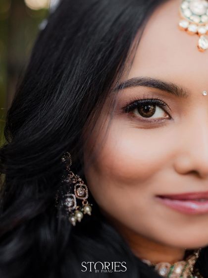 A striking half-face portrait of a bride, focusing on her expressive eyes and delicate makeup. The shot highlights her beautiful jewelry and the quiet confidence in her gaze.
