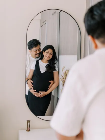 A creative reflection shot capturing the couple's embrace in the mirror. This perspective adds a layer of intimacy and artistry to the home maternity session, showing the moment from a different point of view.
