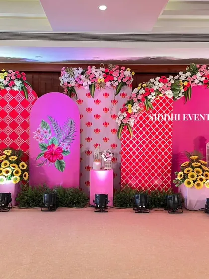 A full view of the Haldi stage, with multiple arched backdrops in shades of pink and red, decorated with floral prints and fresh flower bouquets.