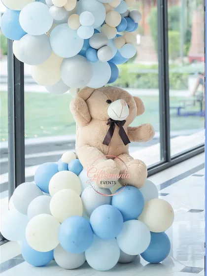 A detailed shot of a teddy bear prop seated on a cloud of blue and white balloons. This type of sculpture can be used as a floor accent or centerpiece.