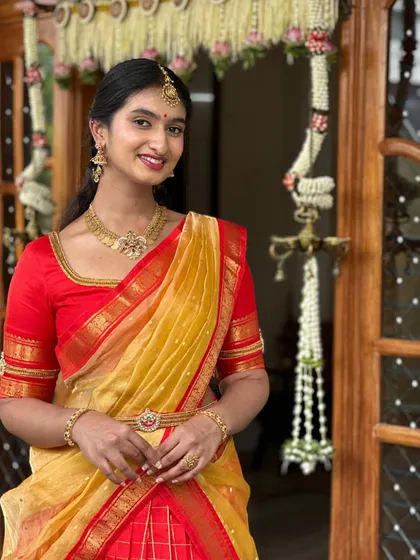 A happy client looking radiant in a custom half saree ensemble. The classic red blouse with a simple Kasu embroidery neckline is designed for festive grace and timeless appeal.