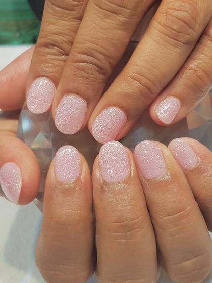 A soft, shimmery pink dip powder manicure on short, natural nails. This service is ideal for anyone looking to grow their nails while enjoying a durable, chip-free color.