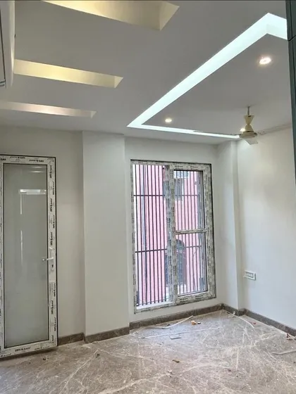 An interior view of a bedroom in the CR Park project, nearing completion. You can see the finished false ceiling with integrated lighting, marble flooring, and newly installed windows, ready for the final touches.
