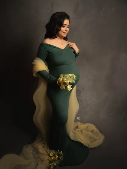 A moment of quiet fulfillment. Holding a delicate bouquet, this mother-to-be looks peaceful and radiant in a classic dark green maternity gown.