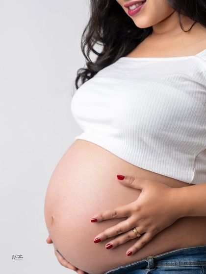 A close-up shot focusing on the beautiful baby bump. This simple, casual style with jeans and a crop top is a popular choice for a relaxed maternity session.