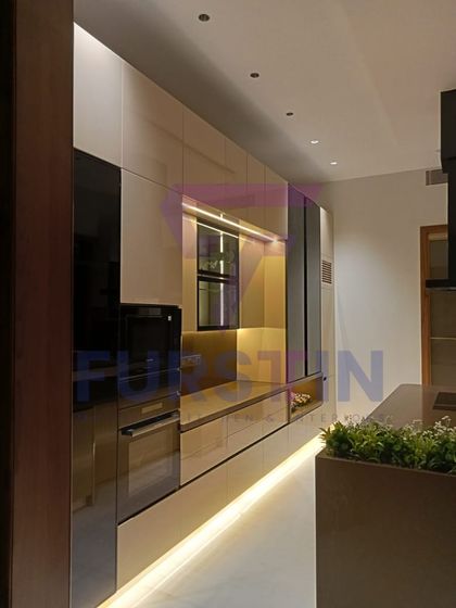 Another angle of the Bharatpur kitchen, highlighting the wall of integrated appliances and storage. The warm under-cabinet and floor-level lighting creates a welcoming ambiance and gives the space a floating effect.